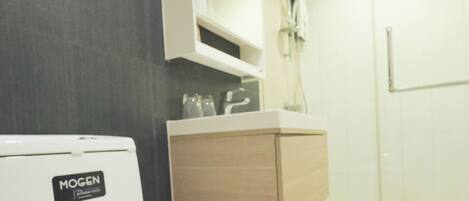 A modern bathroom with a white toilet, a wooden vanity, a glass shower enclosure, and a built-in mirror.