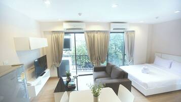 A modern hotel room with a bed, a sofa, a TV, and a desk with a vase of flowers.