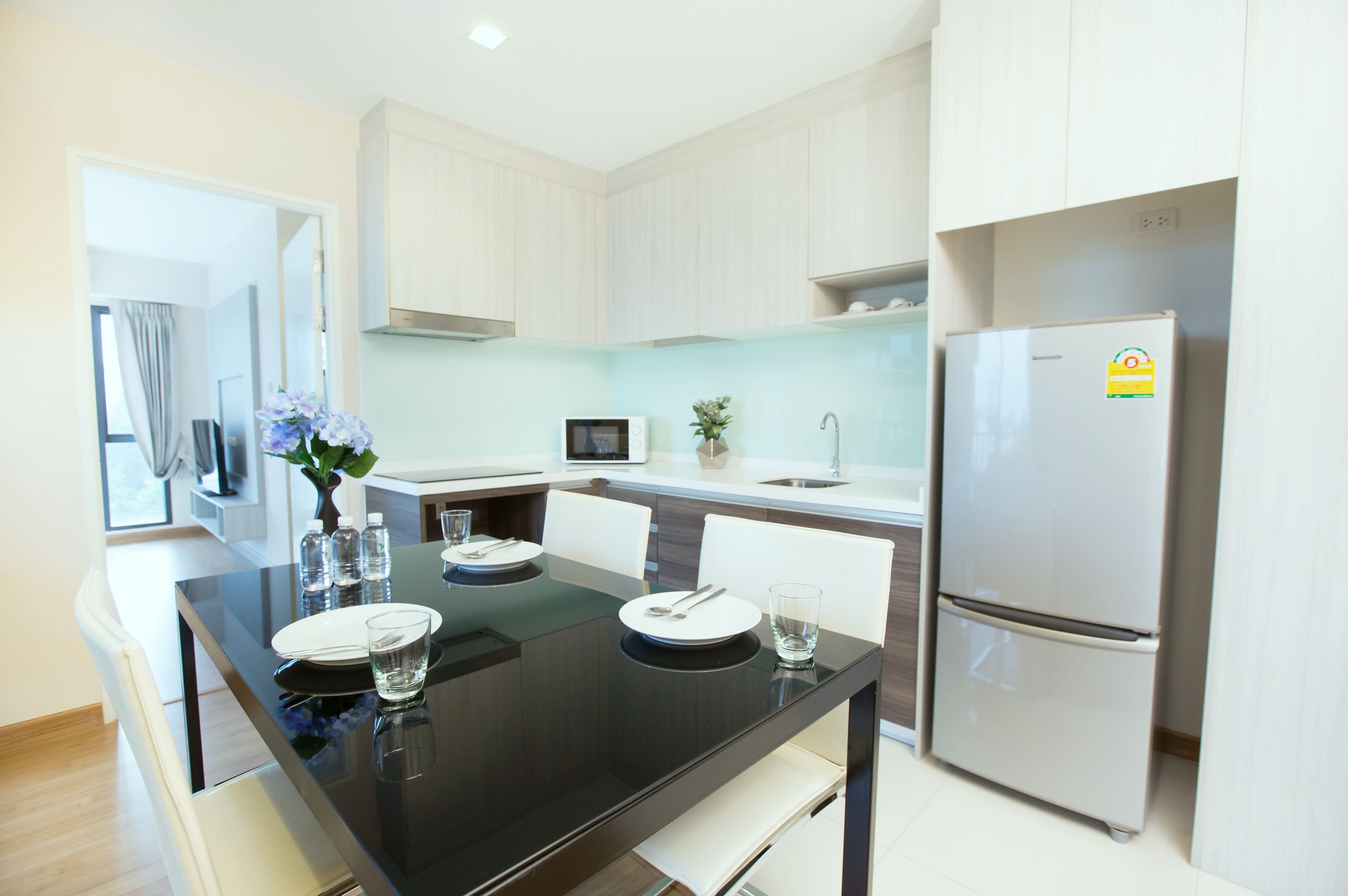 Una cocina moderna con armarios blancos, un comedor con mesa negra y un refrigerador blanco.