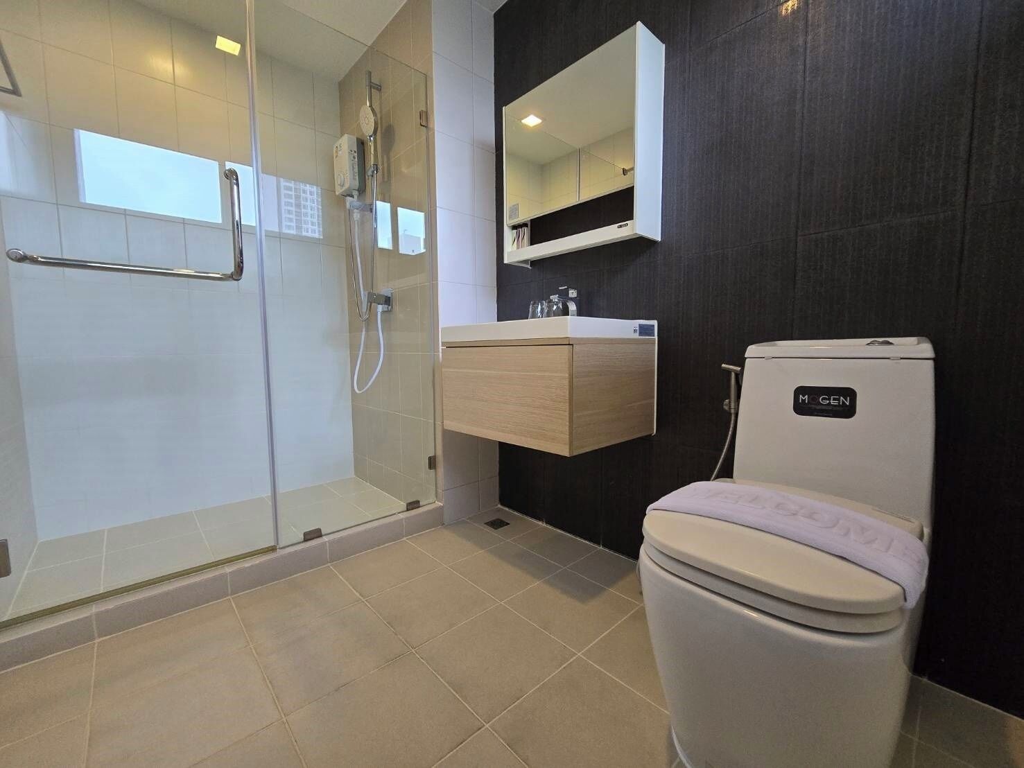A modern bathroom with a glass-enclosed shower, a wooden vanity, a white toilet, and a dark wall.