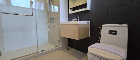 A modern bathroom with a glass-enclosed shower, a wooden vanity, a white toilet, and a dark wall.