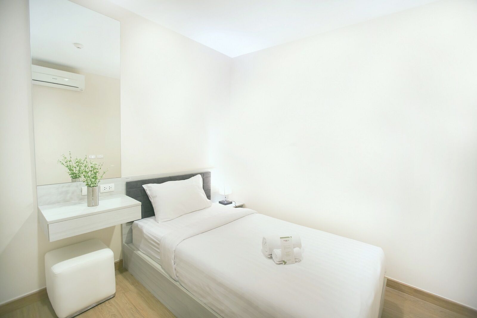A small, clean room with a bed, a bedside table, a mirror, and a small plant.