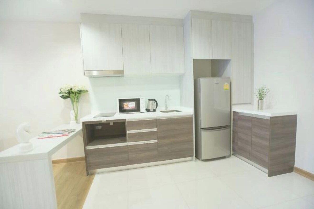 Una cocina moderna con armarios de madera clara, un refrigerador de acero inoxidable y una encimera blanca.