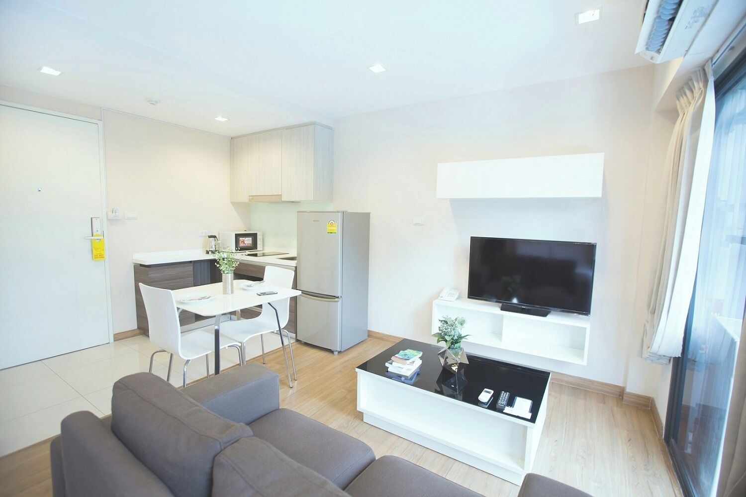 A modern living room with a sofa, a coffee table, a TV, and a kitchen area with a fridge and microwave.