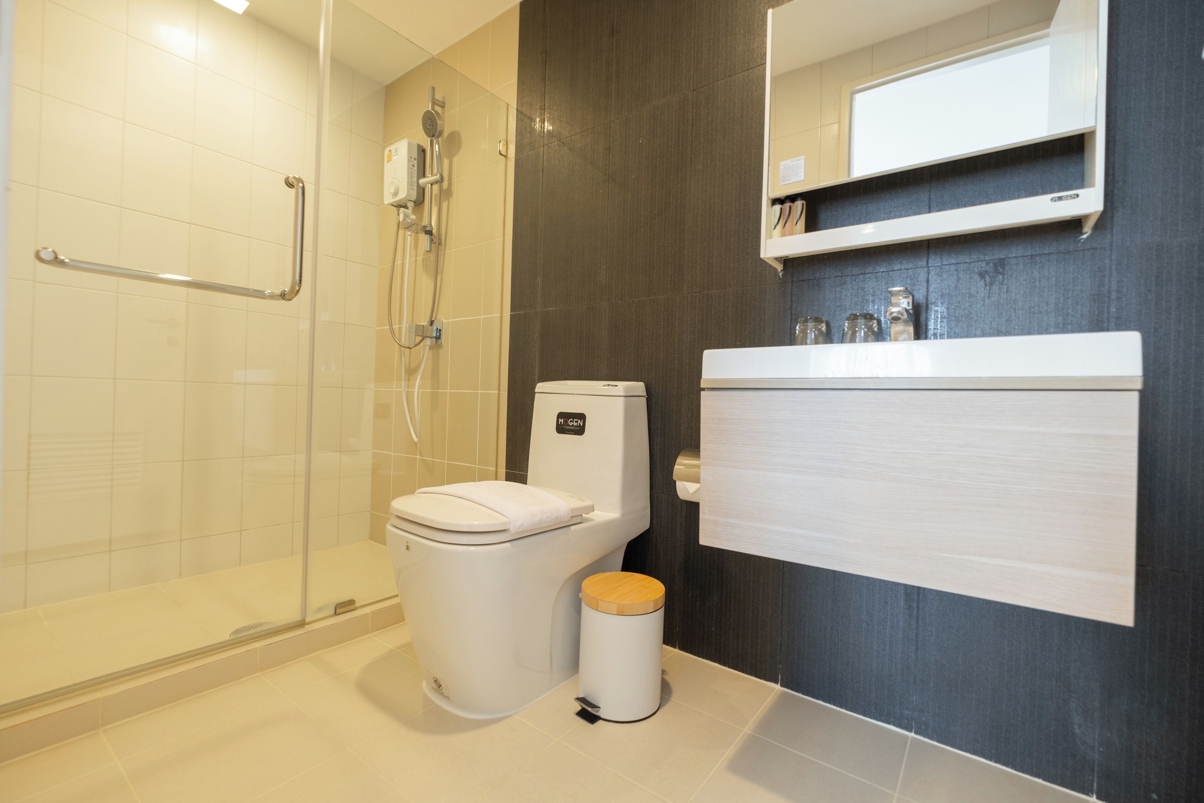 A modern bathroom with a glass shower enclosure, a white toilet, and a wooden waste bin.