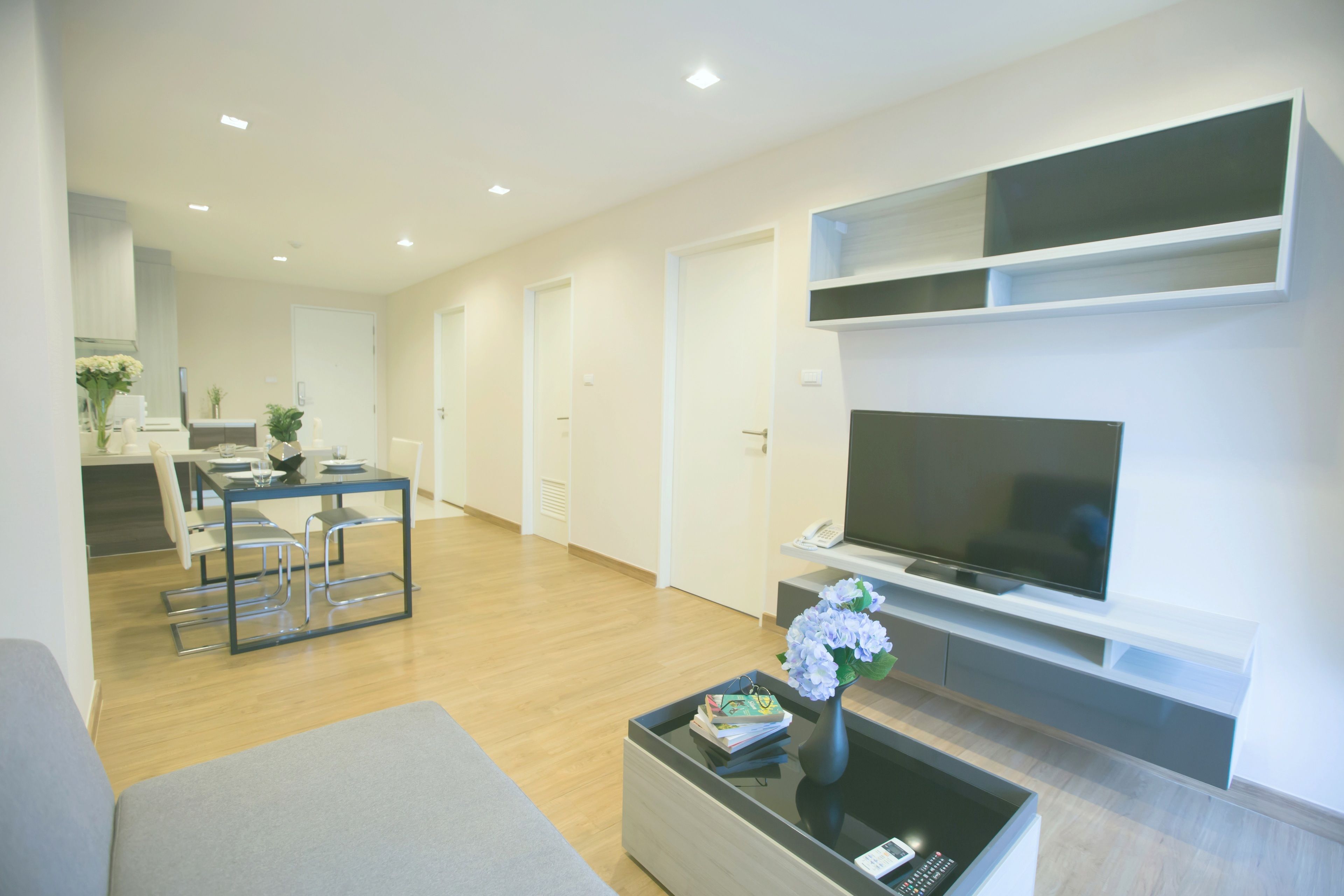 A modern living room with a flat-screen TV, a coffee table with a vase, and a dining area with chairs and a table.