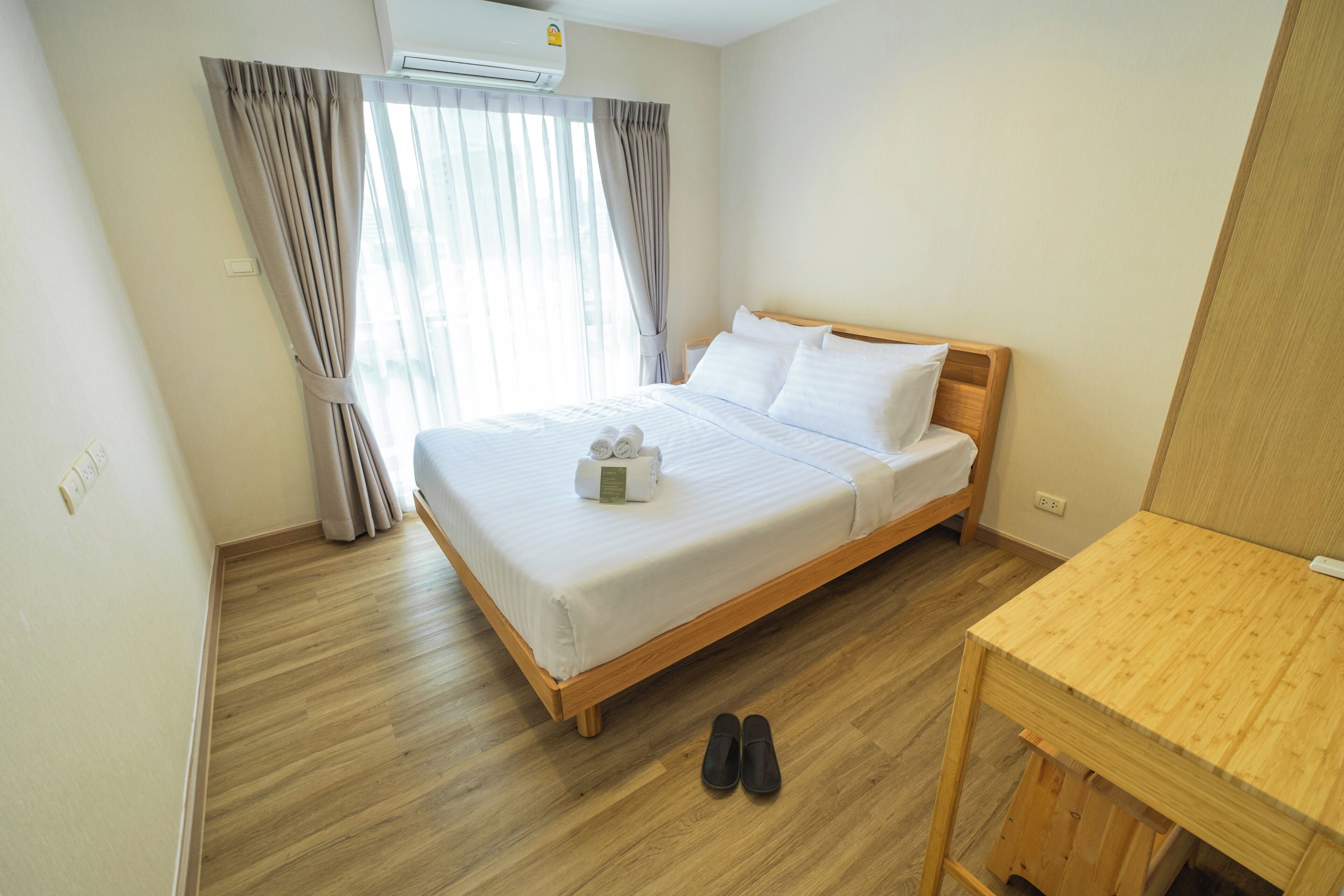 A hotel room with a wooden bed, white linens, a wooden nightstand, and a wooden table.
