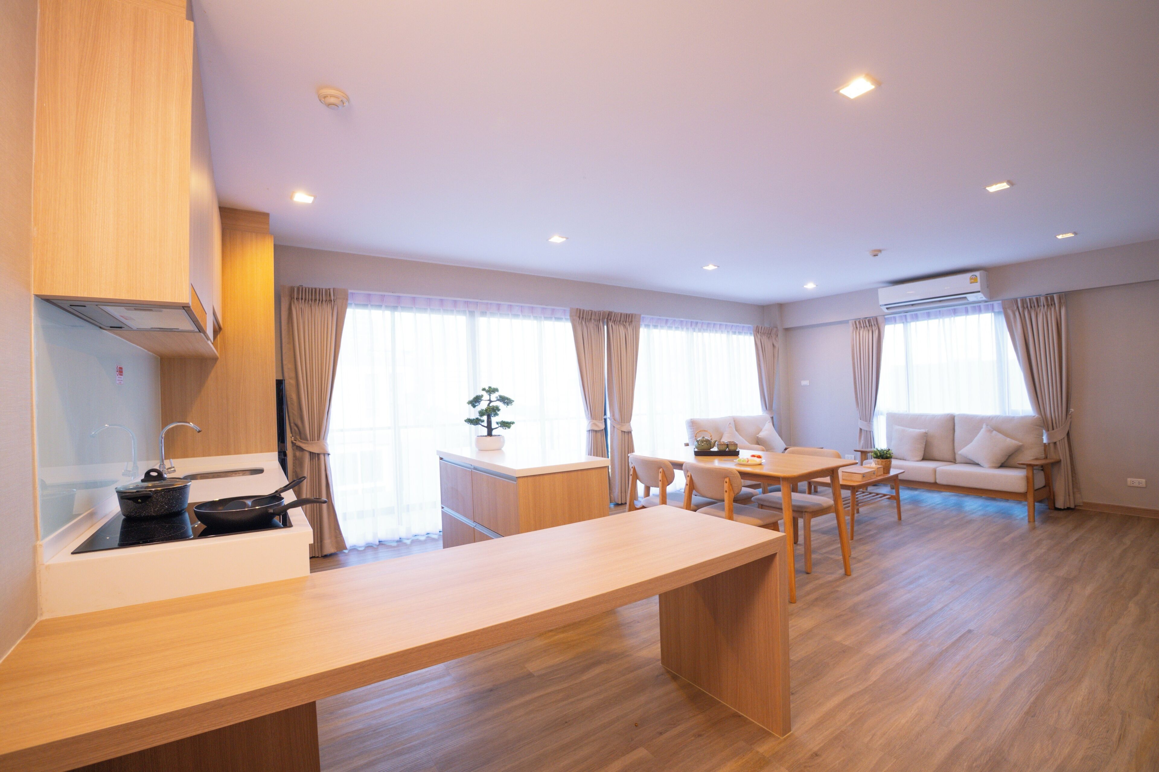 A modern kitchen with a built-in stove, a dining table, and a sofa in a bright living area with large windows.