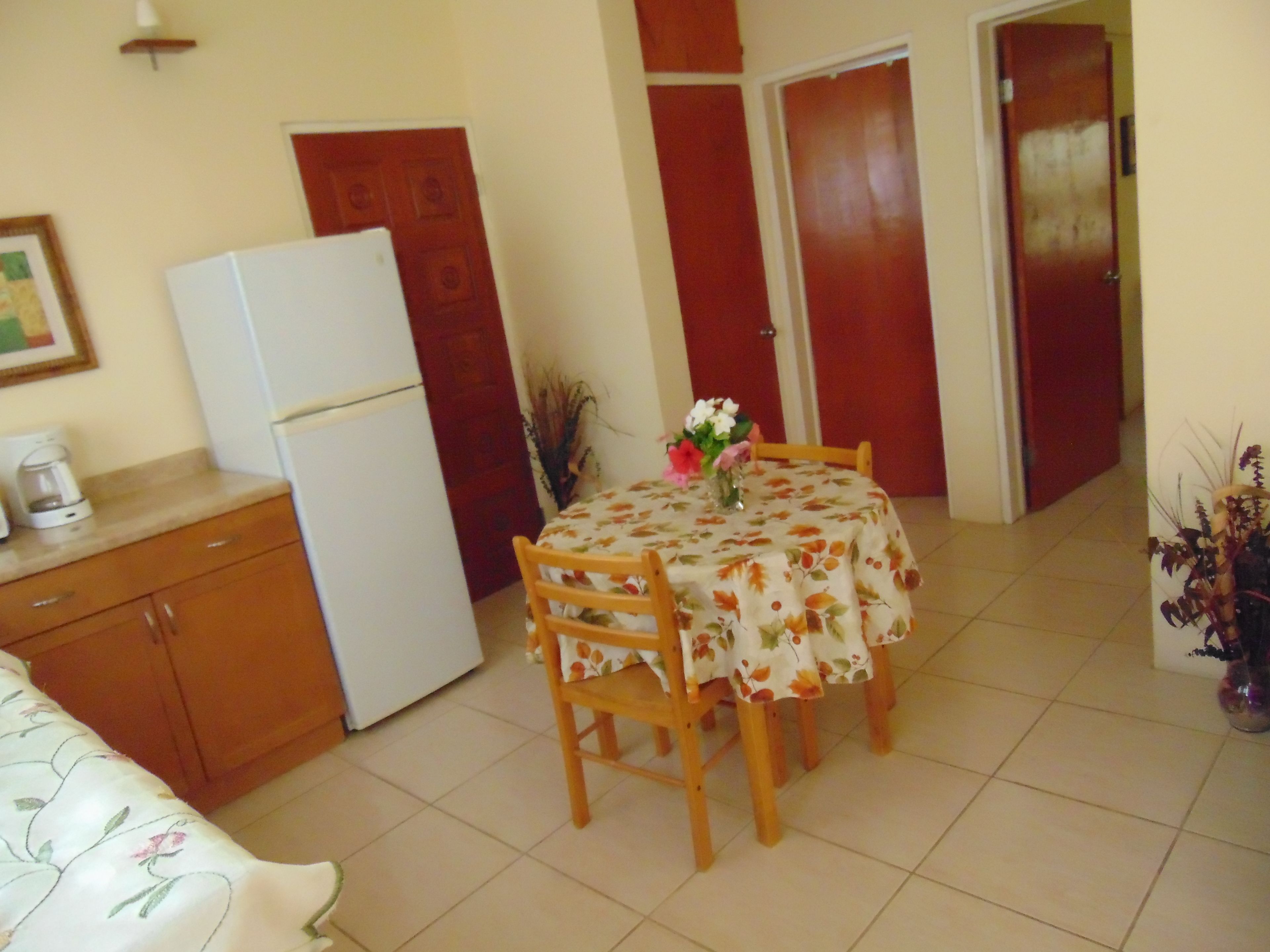 Una cocina pequeña con un refrigerador, una mesa de comedor con sillas y una cafetera en la encimera.