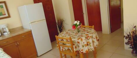 Una cocina pequeña con un refrigerador, una mesa de comedor con sillas y una cafetera en la encimera.