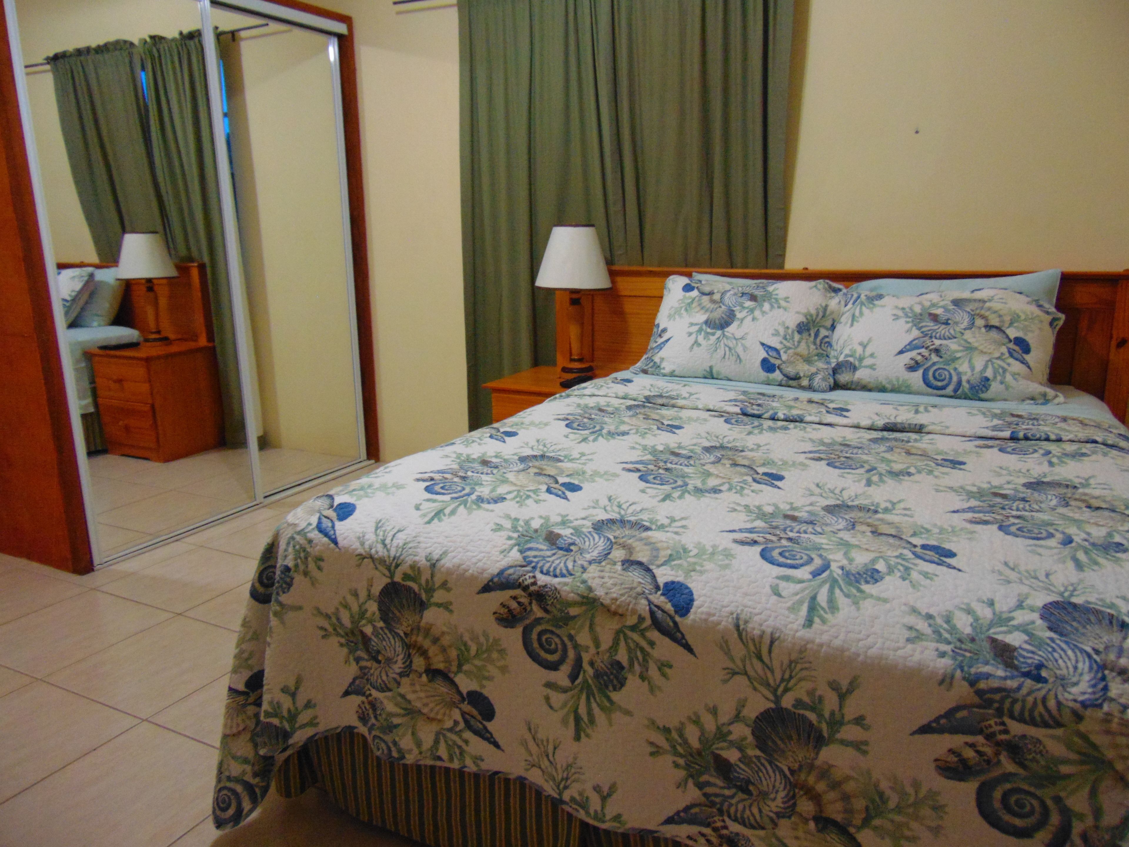 A bedroom with a bed, a nightstand, a mirror, and a dresser.
