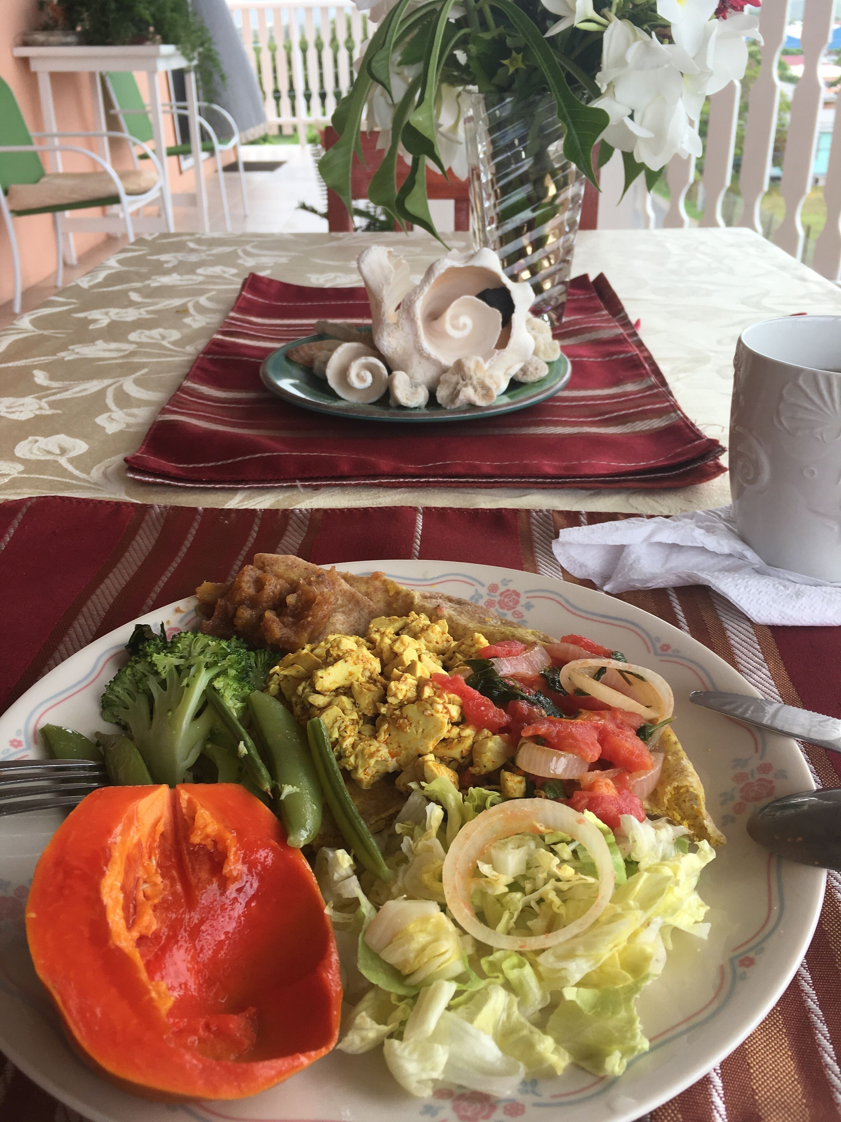 Una mesa de comedor con un plato de comida, una taza y un jarrón decorativo.