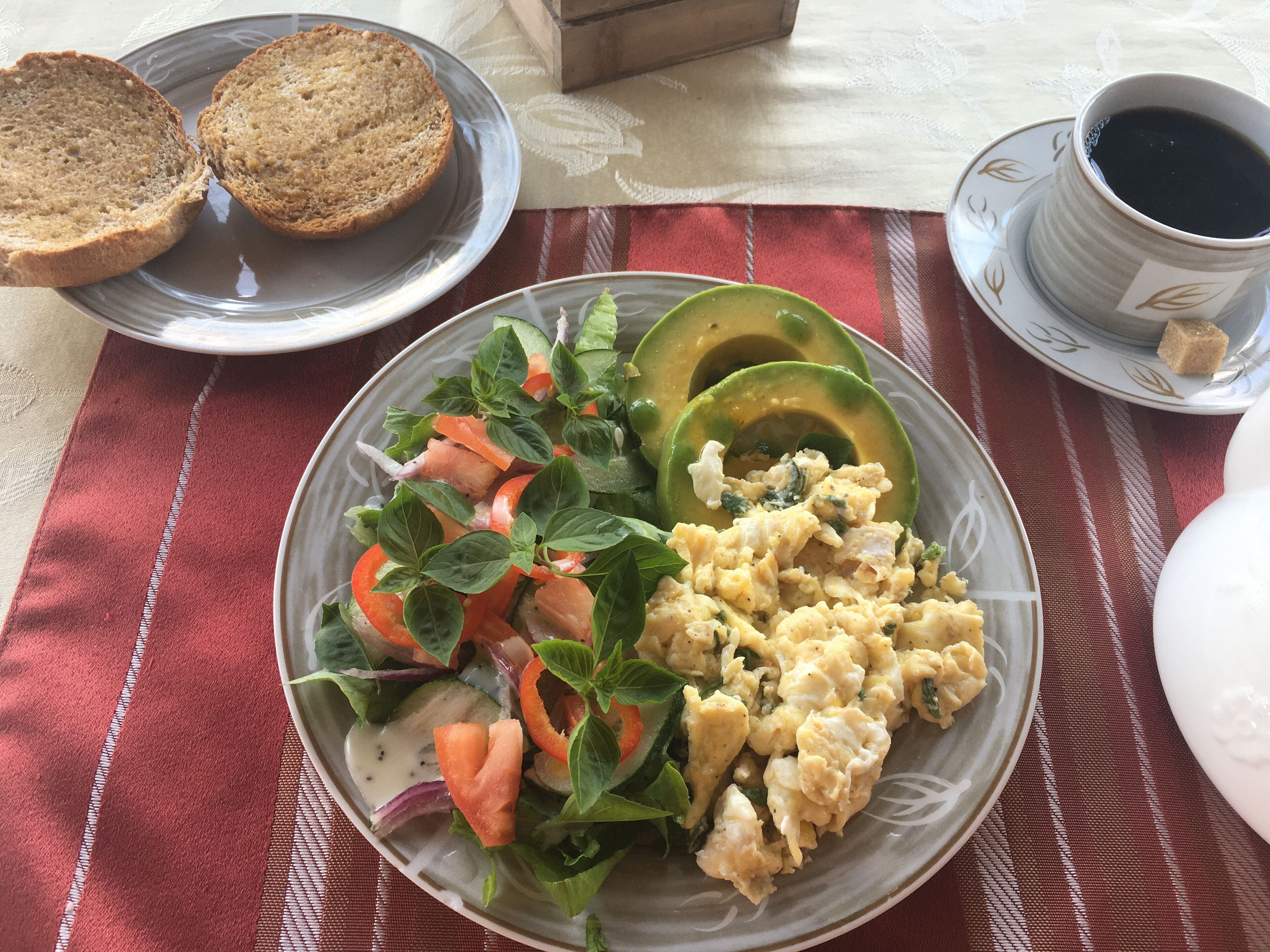 En tallrik med rörägg, skivor av avokado och en blandad grönsallad står på ett bord med en röd- och vitrutig duk.