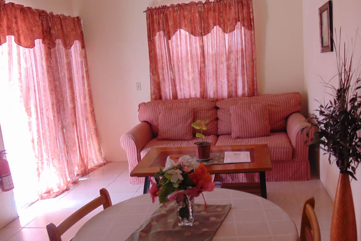A living room with a sofa, a coffee table with a vase of flowers, and a dining table with chairs.