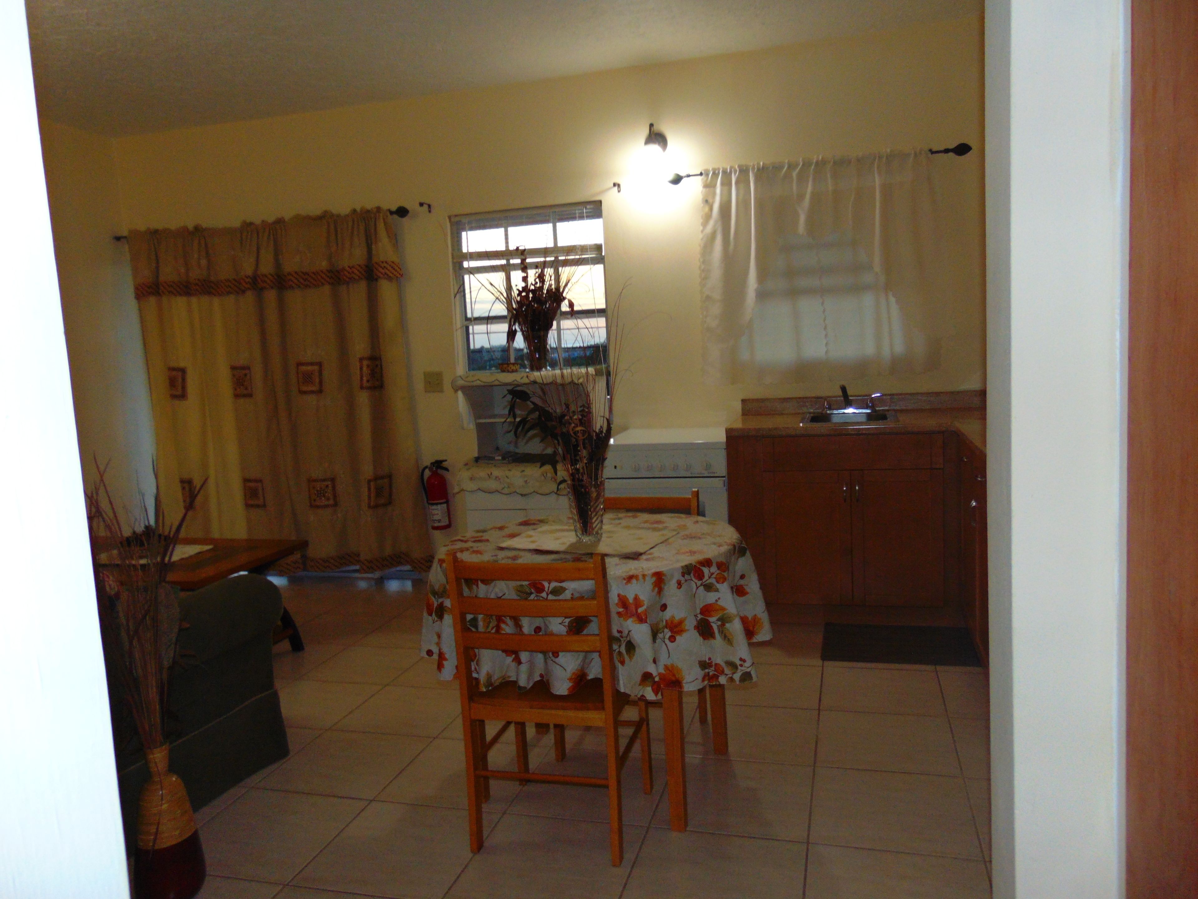 A dining area with a table set for four, a window with curtains, a kitchen area with cabinets, and a fire extinguisher on the wall.