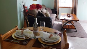 A dining area with a wooden table set for four, a vase with red flowers, and a framed picture on the wall. - Antigua Seaview (St. John's)