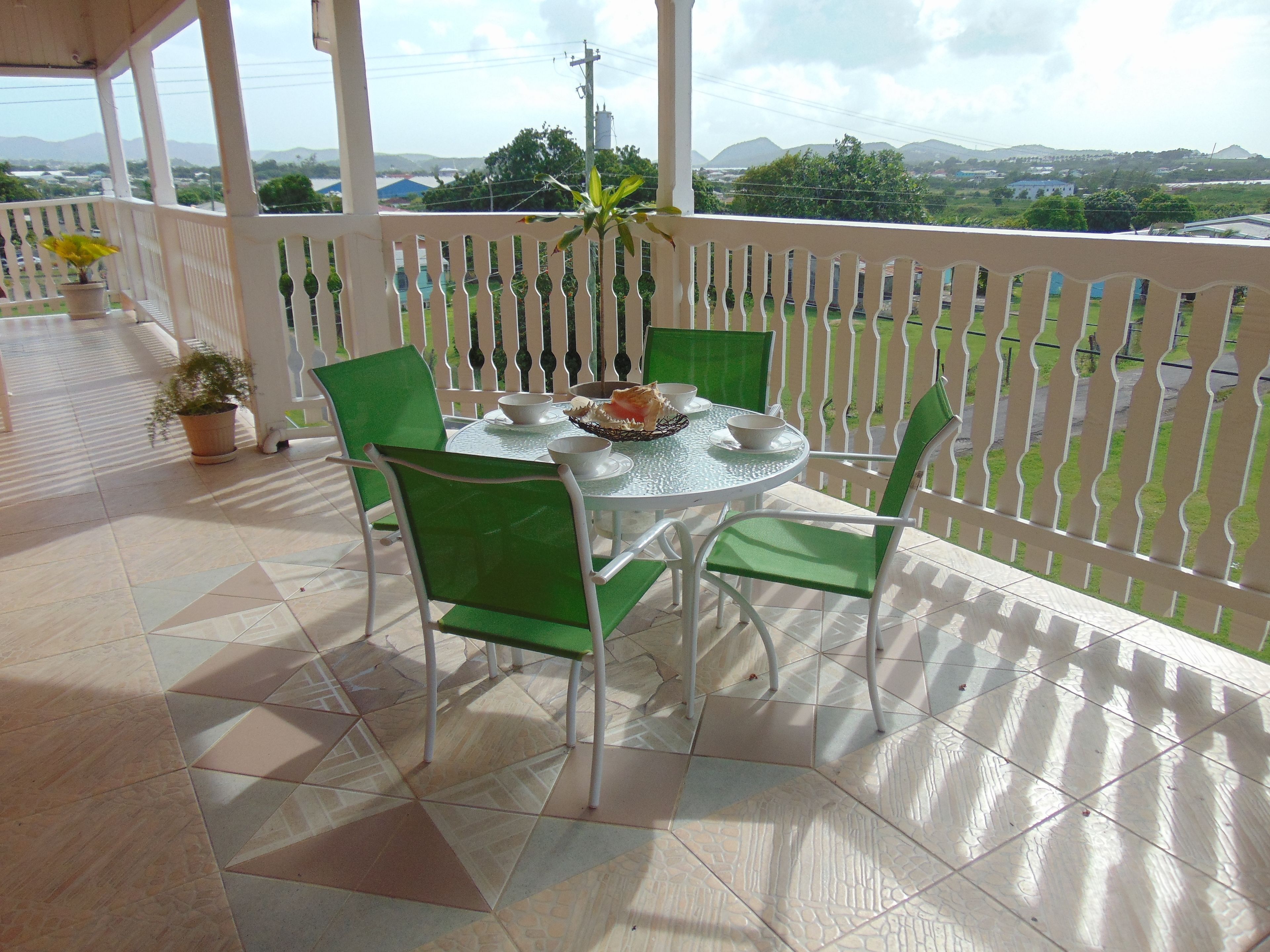 A covered outdoor dining area with a table and chairs, a potted plant, and a view of the landscape.