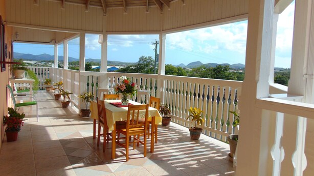 A covered outdoor area with a table and chairs, surrounded by potted plants, and overlooking a scenic landscape. - Antigua Seaview (St. John's)