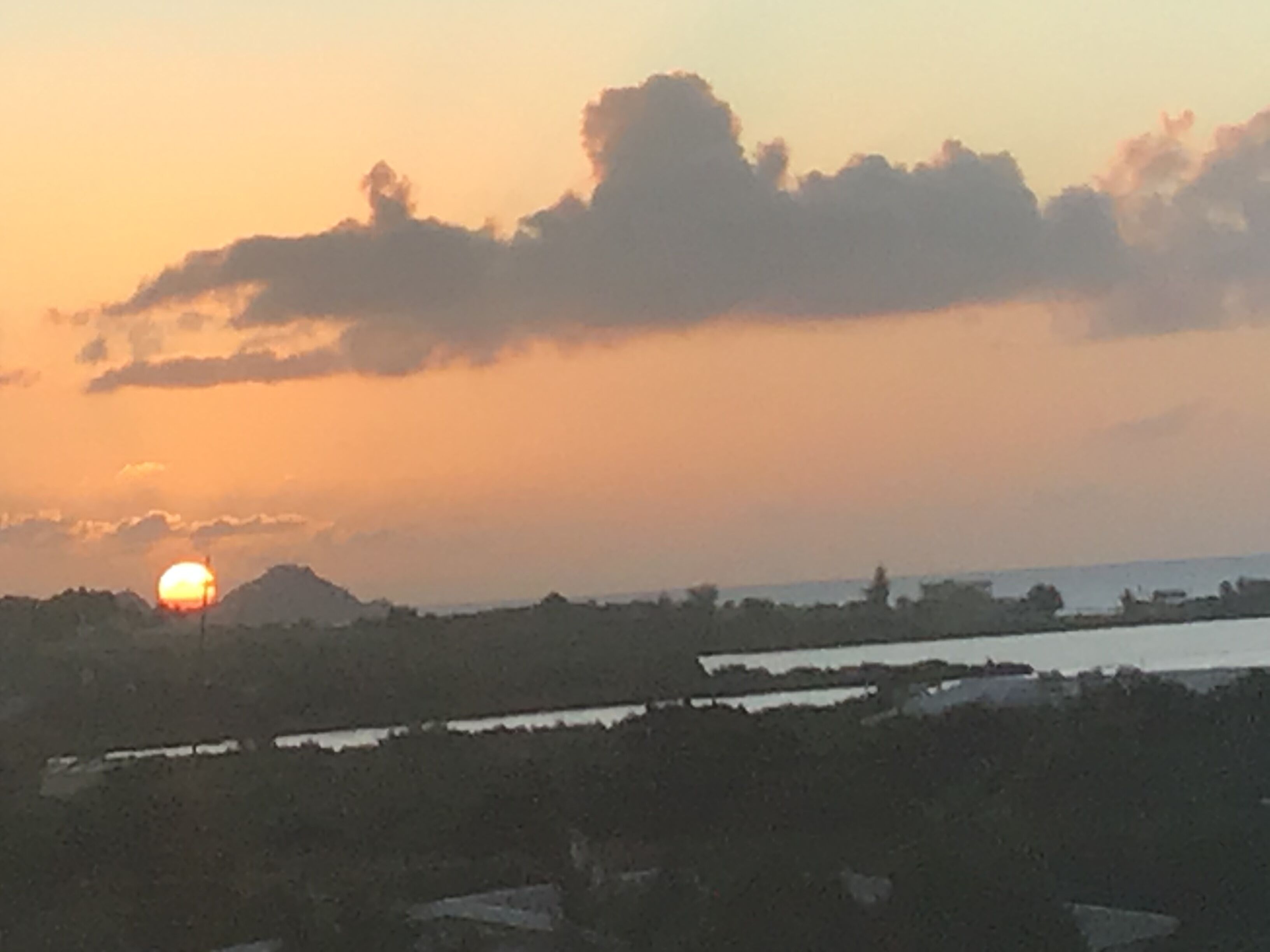 A sunset over a landscape with a body of water and distant hills.