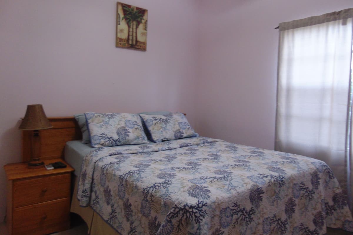 A bedroom with a bed, a nightstand, a lamp, and a painting on the wall.