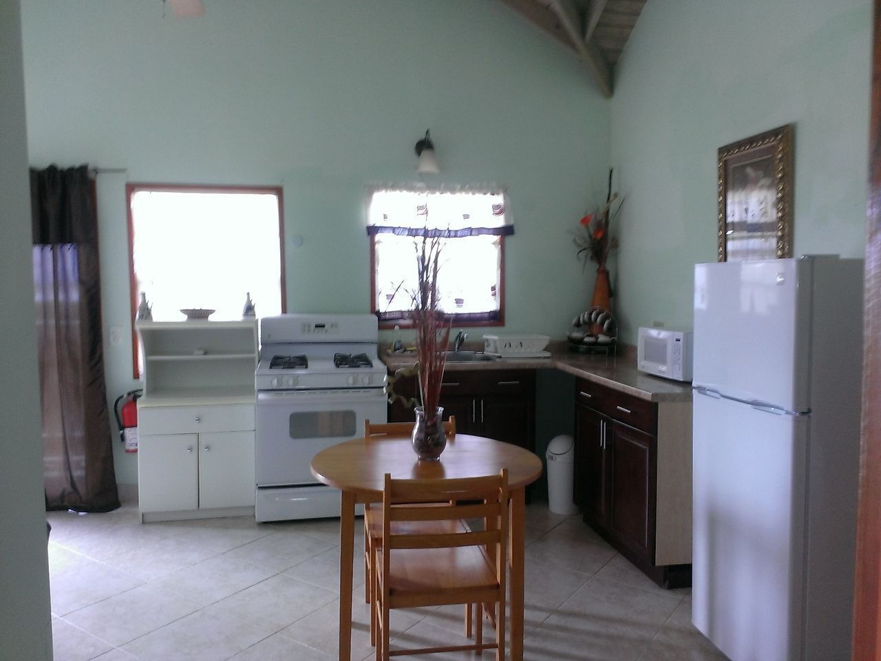 Une cuisine équipée d’une table à manger, de chaises, d’une cuisinière, d’un réfrigérateur et d’une fenêtre avec des rideaux.