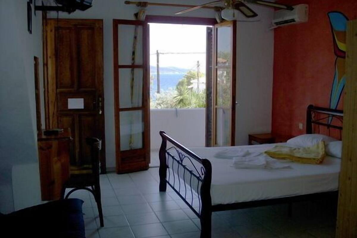 A bedroom with a bed, a desk, and a view of the outdoors.