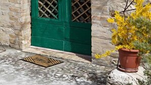 A stone building with a green arched door, a small window above the door, and a potted plant with yellow flowers in front. - Subretia Residenze di Campagna (Montefalco)