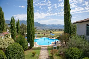 A swimming pool surrounded by tall cypress trees, with a view of distant mountains and a white building with a tiled roof. - Subretia Residenze di Campagna (Montefalco)