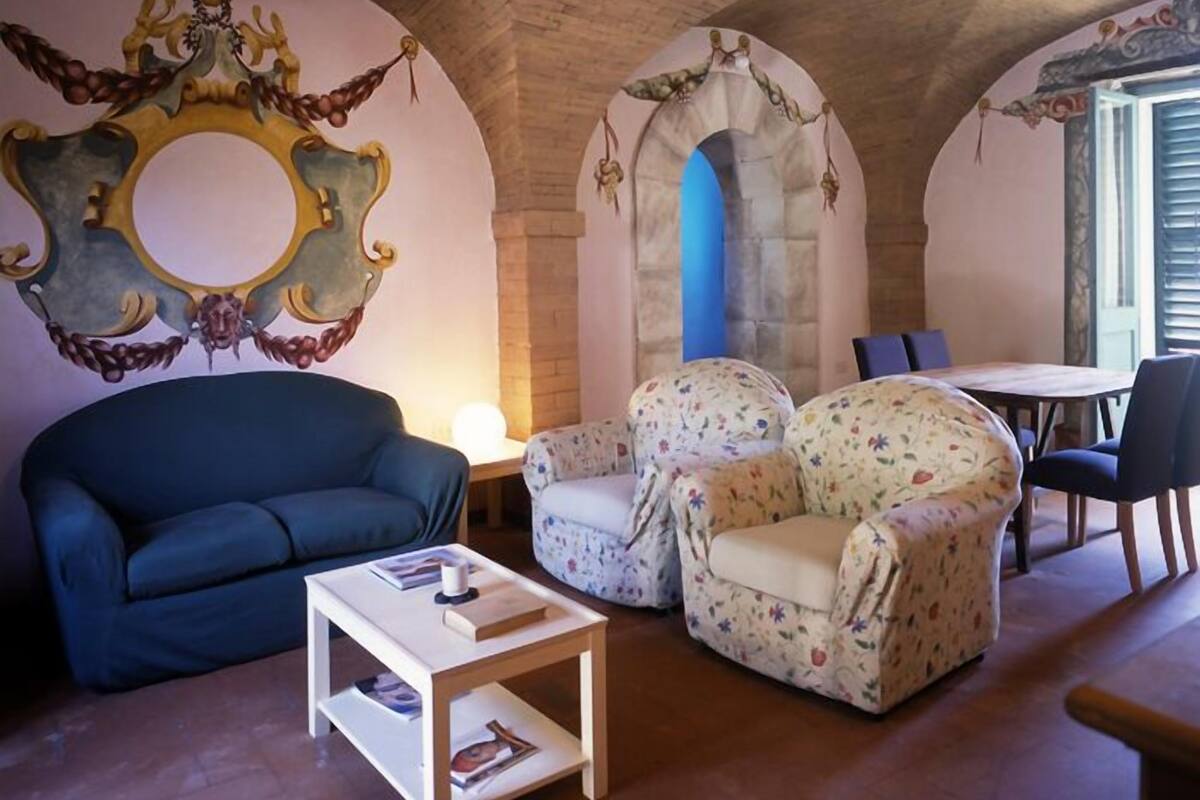 Un salon chaleureux avec un canapé bleu, des fauteuils à motifs floraux, une petite table basse et un miroir décoratif accroché au mur.
