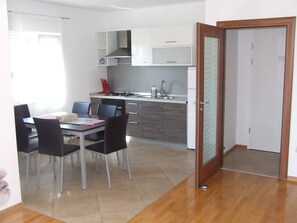 Eine moderne Küche mit weißen Schränken, einem Gasherd und einer Spüle. Ein Esstisch mit Stühlen und ein Fenster mit Vorhängen sind ebenfalls vorhanden.