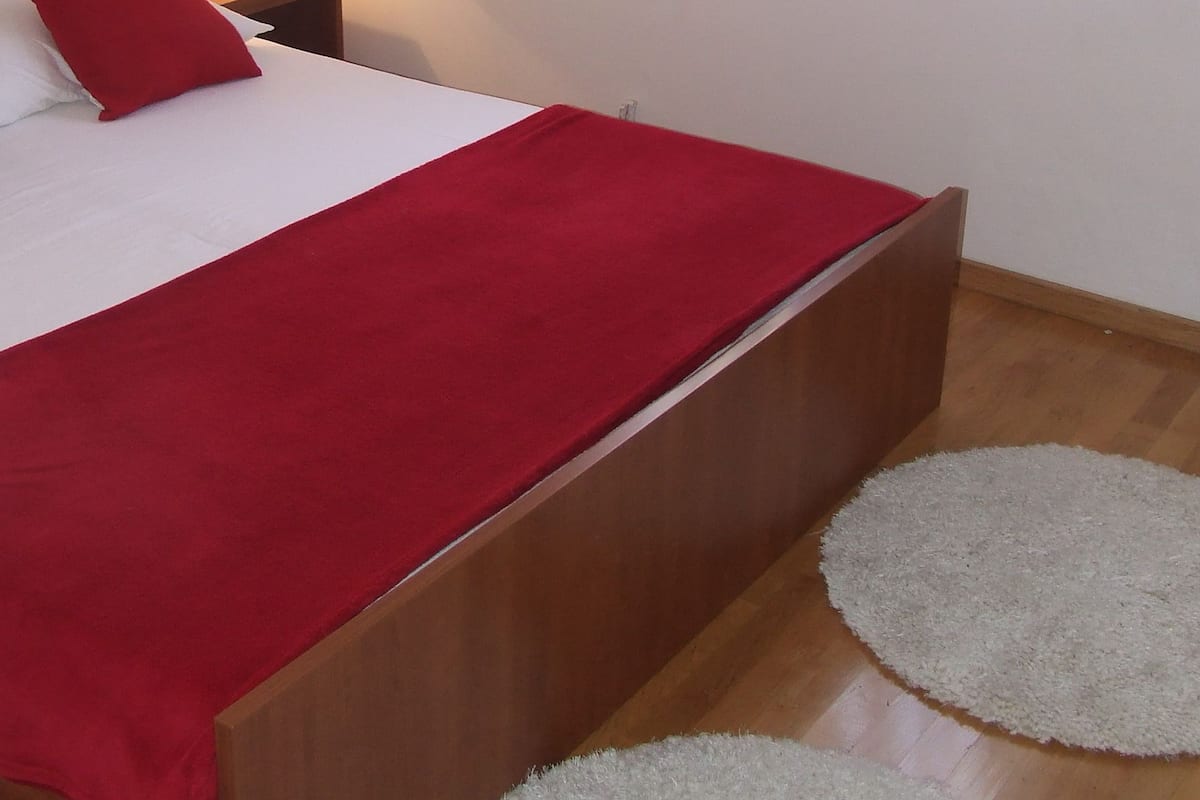 A neatly made bed with a red blanket, a bedside lamp, and a small nightstand with a lamp.
