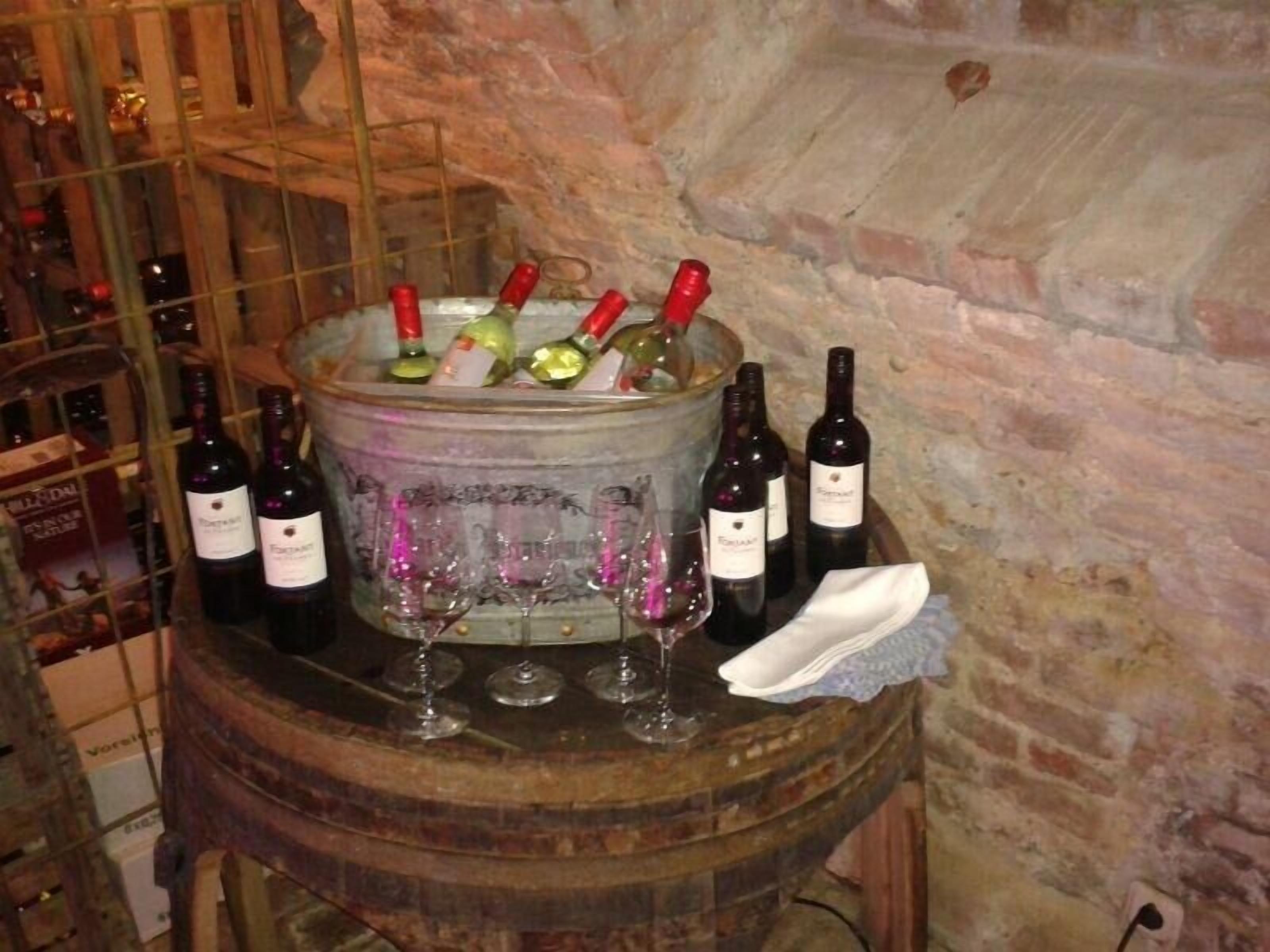 A wooden barrel with wine bottles and glasses, set against a brick wall.