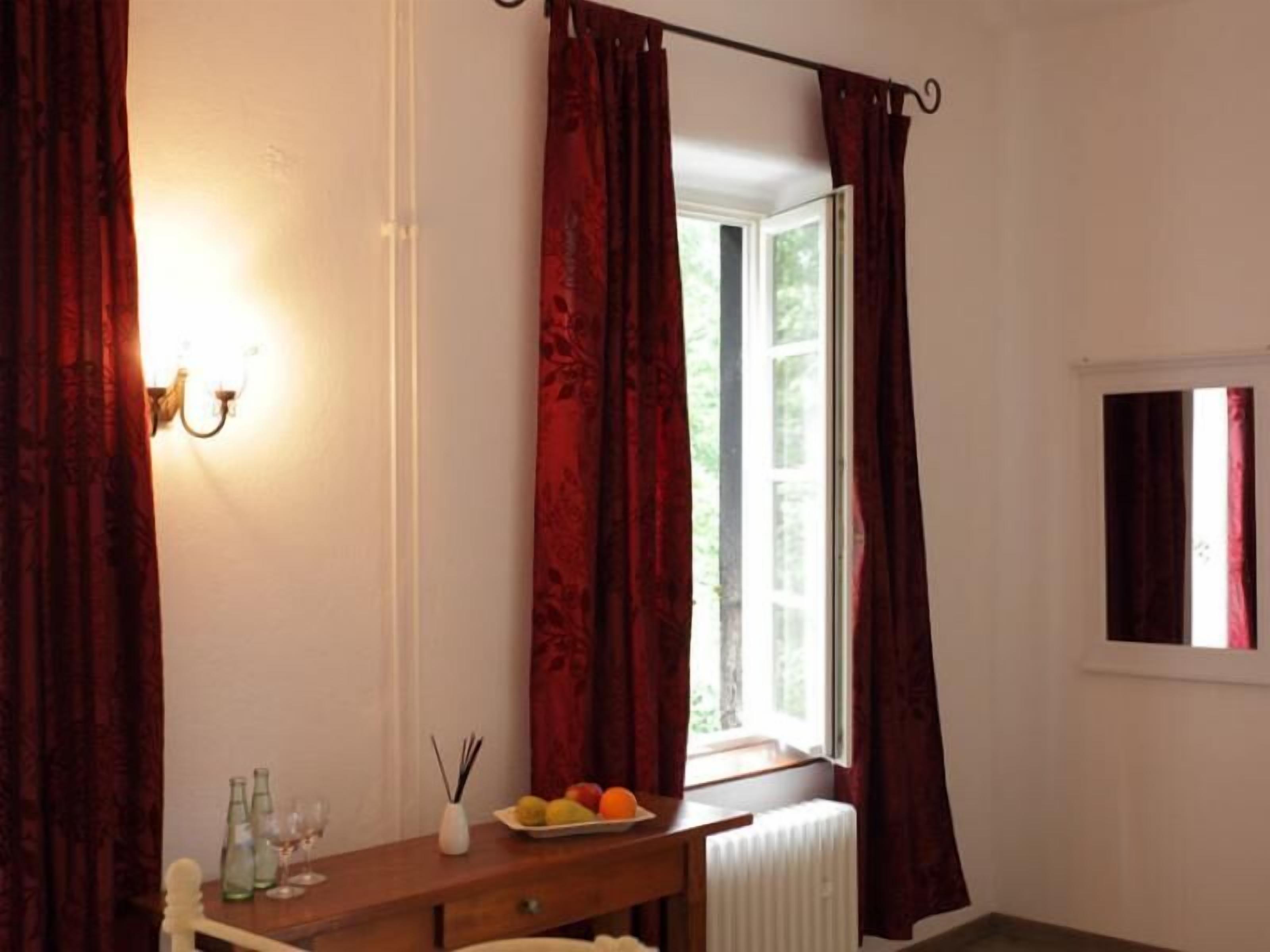A room with a wooden desk, a radiator, and a window with red curtains.