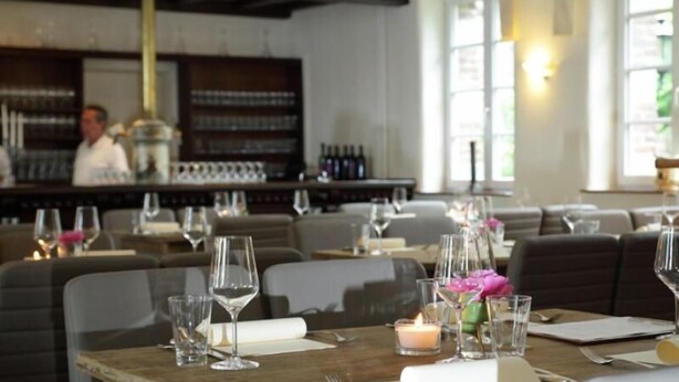 A restaurant interior with tables set for dining, a bar area in the background, and a candle on the table. - Das Dycker Weinhaus (Juechen)