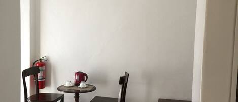 A small, well-lit room with a round table and two chairs, a fire extinguisher on the wall, and a small cabinet.