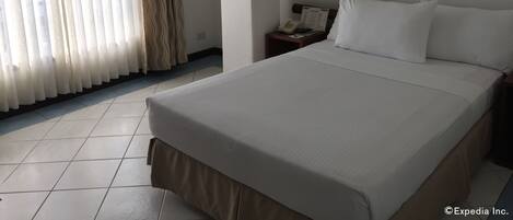Una habitación de hotel con una cama grande, una mesita de noche con lámpara, un teléfono y un aire acondicionado de pared.