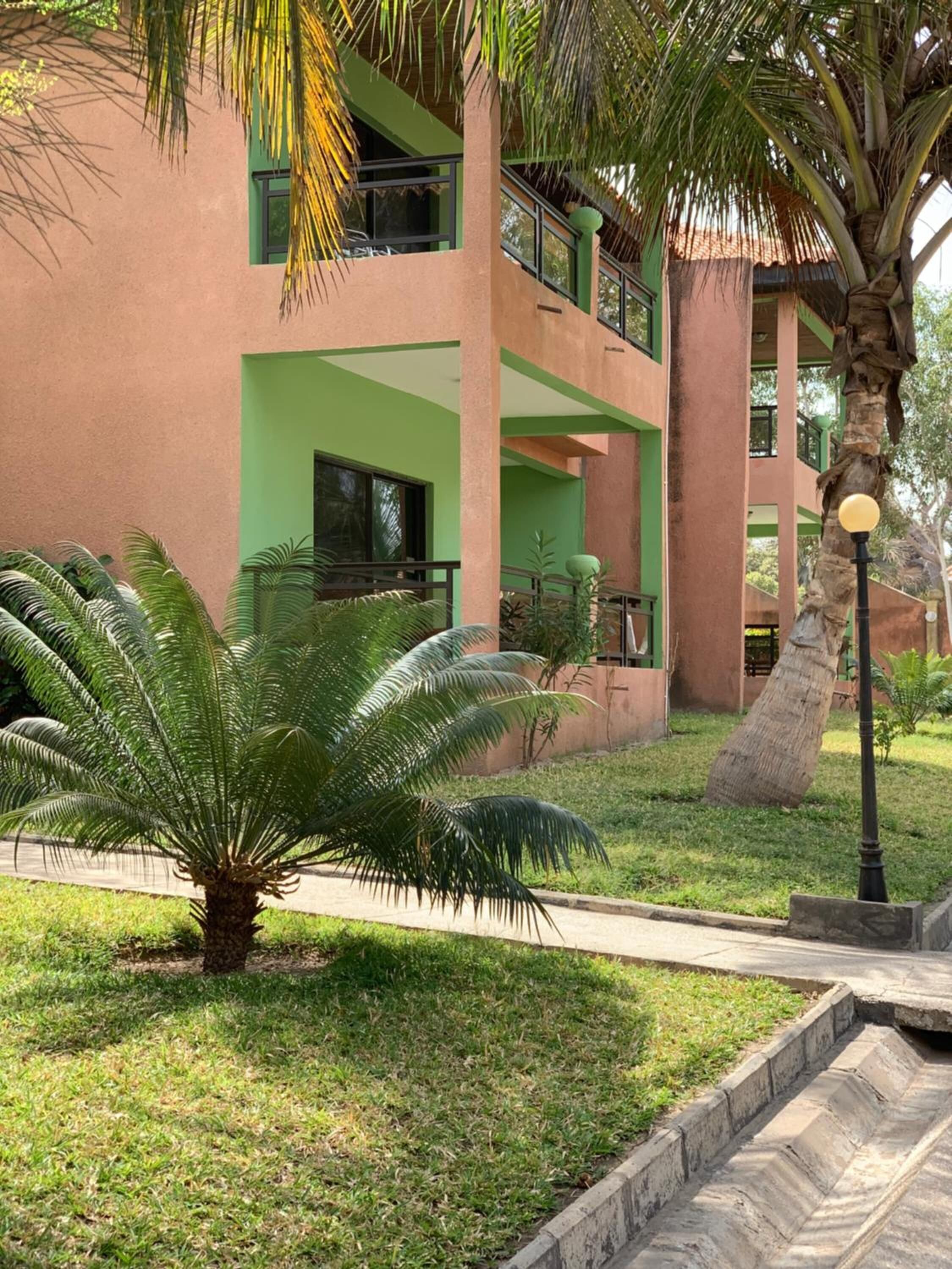 A multi-story building with green and pink exterior walls, a palm tree, and a well-maintained lawn.