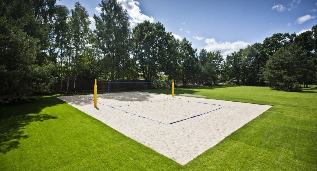 A volleyball court with a net, surrounded by green grass and trees.