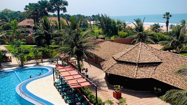 Piscina de diseño curvo en un resort, rodeada de sillones de descanso y sombrillas, con vista a la playa y al océano.