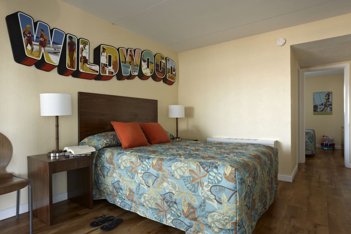 A bedroom with a bed, two bedside tables, a lamp, and a wall sign.
