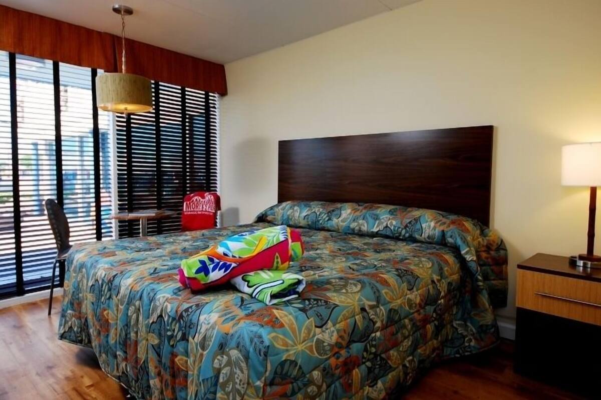 A hotel room with a large bed, a wooden headboard, a desk, and a chair.