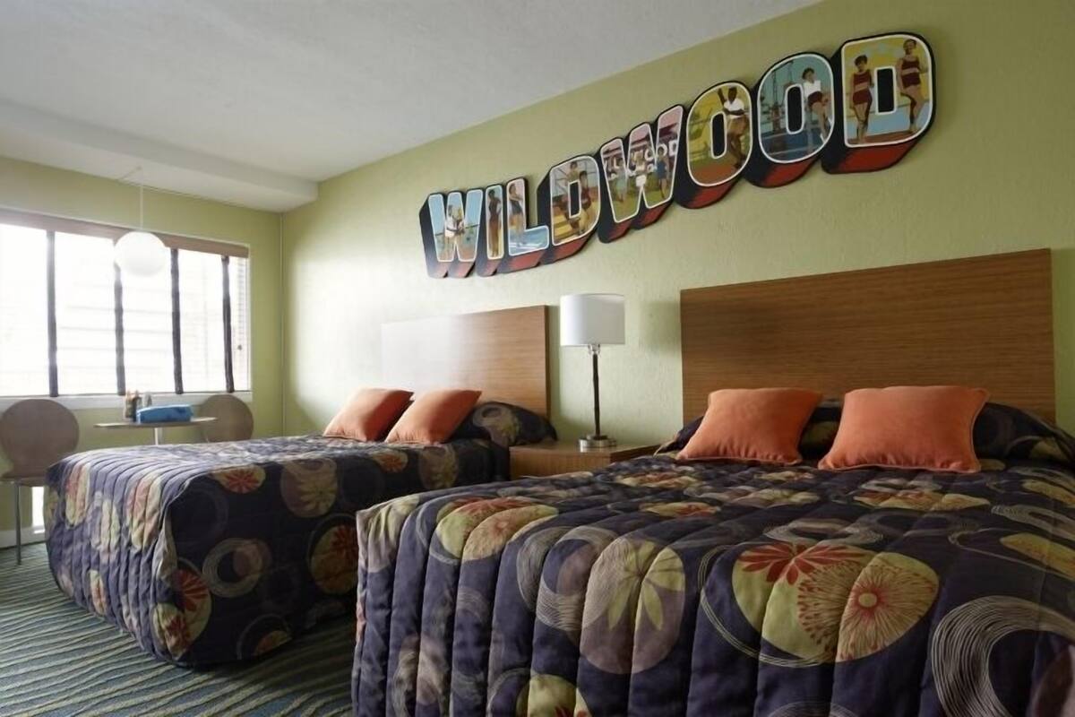 A hotel room with two beds, a large window, and a wall sign that reads "WILDWOOD".
