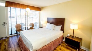 Habitación de hotel con una cama grande, una mesita de noche con lámpara, una silla y vistas por la ventana.