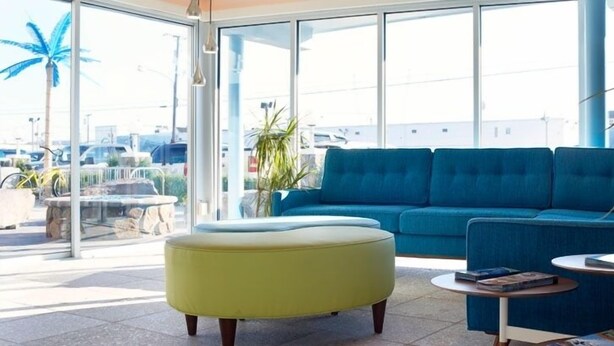 Un espacio lounge moderno con un sofá azul, un otoman amarillo y una pequeña mesa redonda con libros.