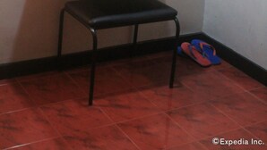 A bathroom with a wooden-framed mirror, a sink with stacked white towels, a black chair, and red slippers on the floor. - Halina Drive Inn Hotel - Pasay (Pasay)