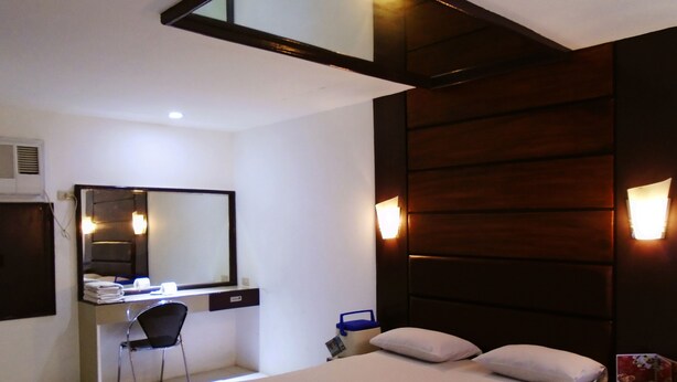 A hotel room with a bed, a desk with a chair, a mirror, and wall-mounted lights. - Halina Drive Inn Hotel - Pasay (Pasay)