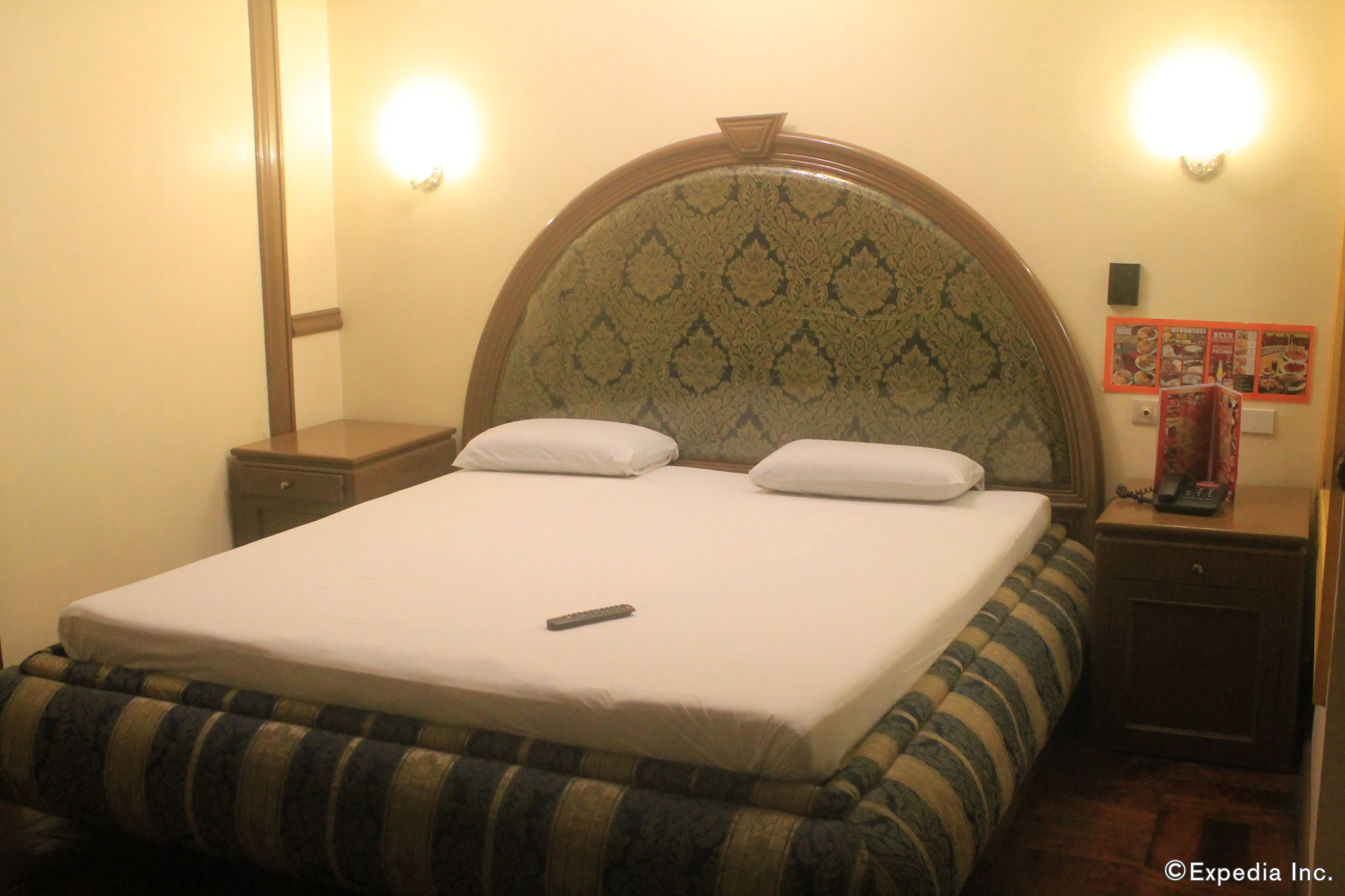 A hotel room with a bed, a nightstand, a lamp, and a wall-mounted light fixture.