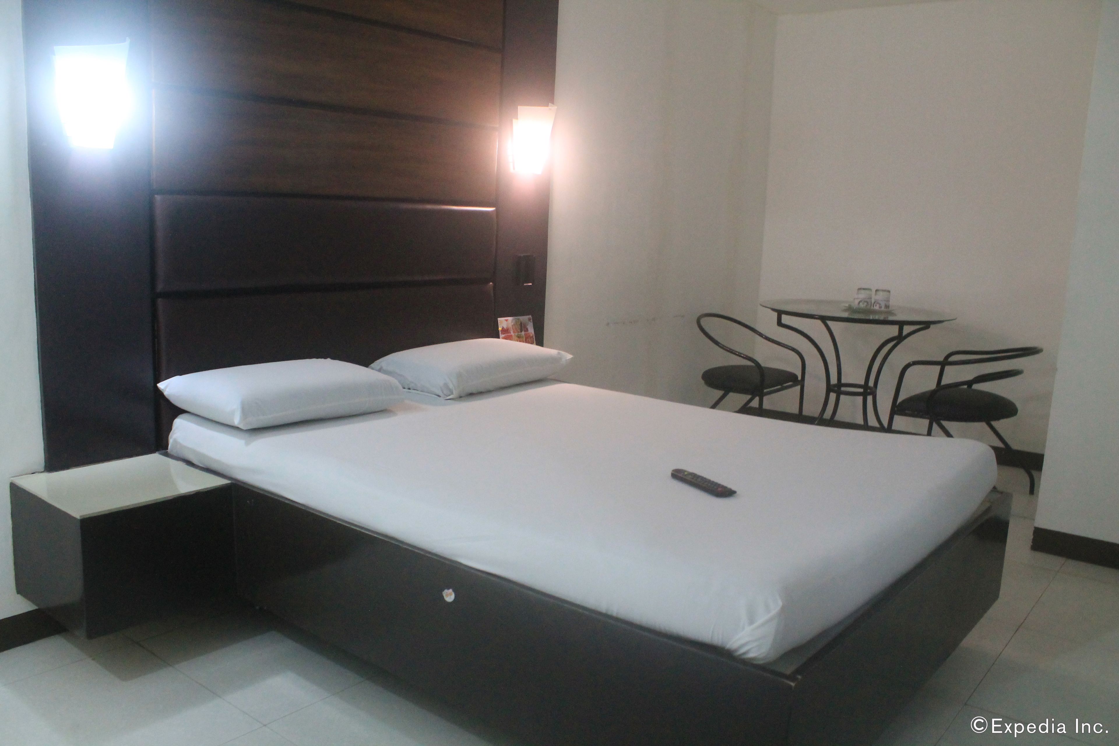 A modern hotel room with a large bed, bedside tables, a small round table with chairs, and two wall-mounted lights.