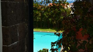 A view through a window of a swimming pool surrounded by greenery and a clear sky. - Convento de São Francisco (Vila Franca do Campo)