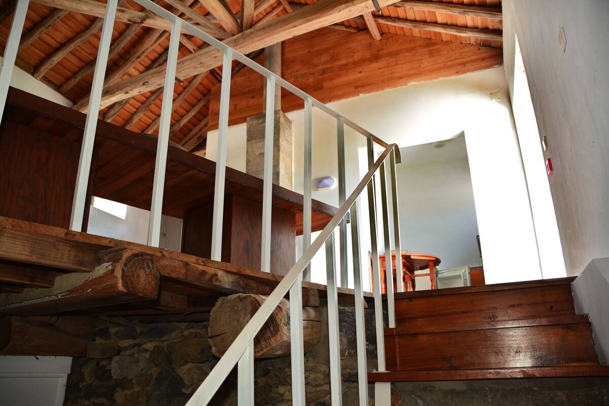 Eine Holztreppe mit steinernen Wangen, weißen Geländern und einer rustikalen Decke.